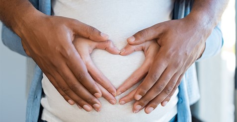 man and woman's hands formed in a heart-shape on pregnant belly